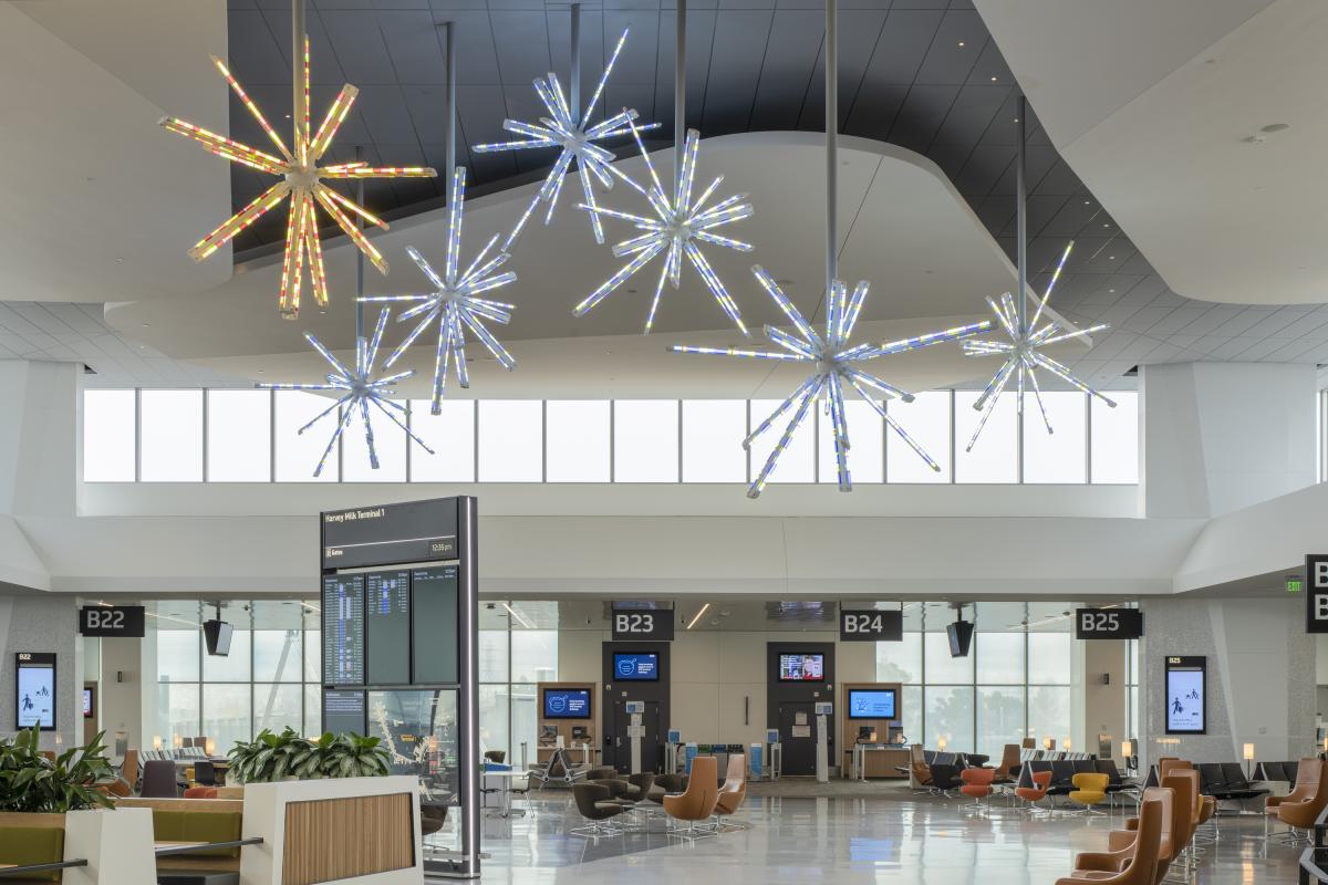 A  suspended light installation by Spencer Finch. The installation features 7 starburst shaped illuminated sculptures, light in blue and yellow, suspended over a seating area at SFO. 