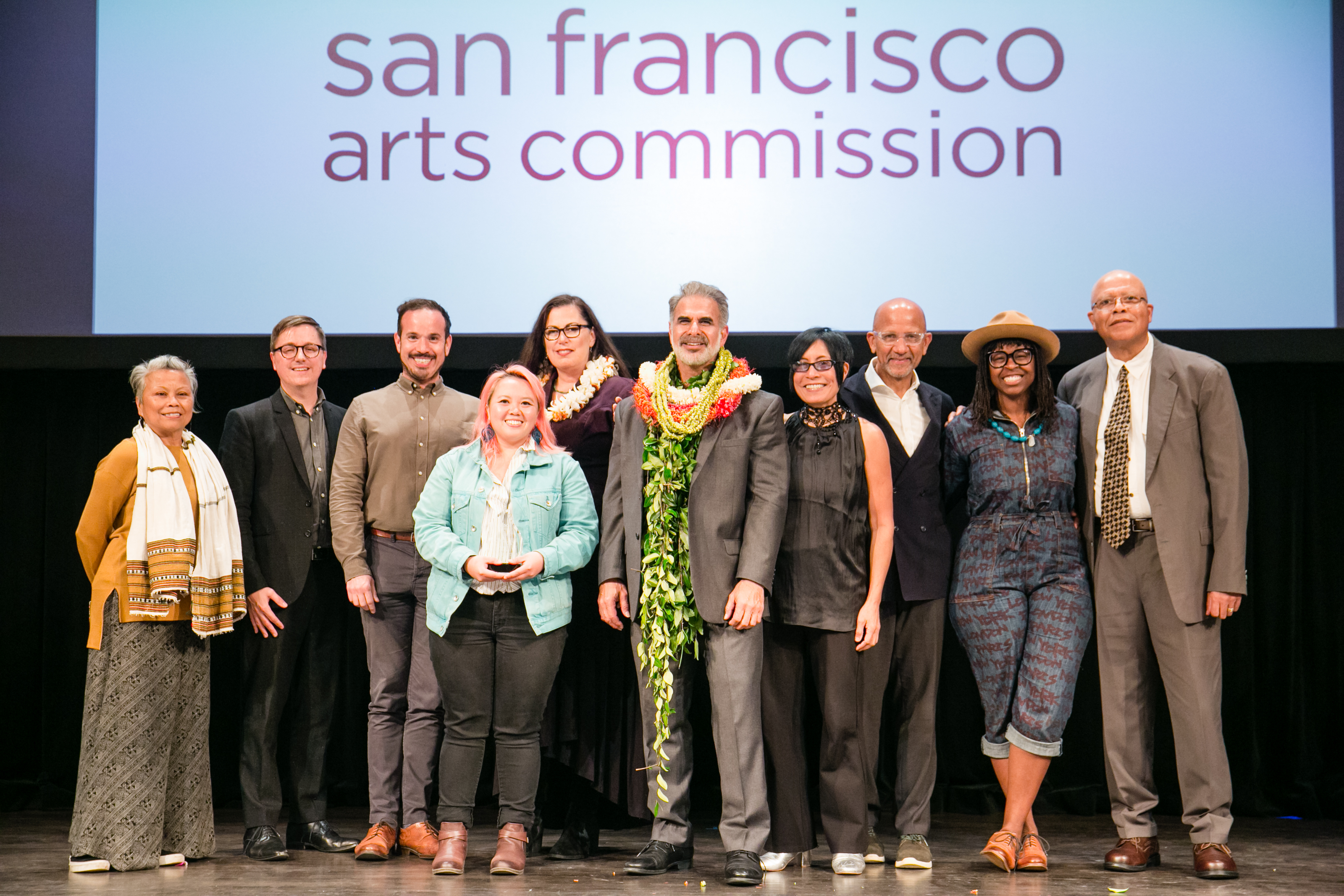 Grant Convening Info Commissioners, awardees, staff and special guests posing on stage in a group photo at the 4th Annual Grants Convening. Photo: Andria Lo