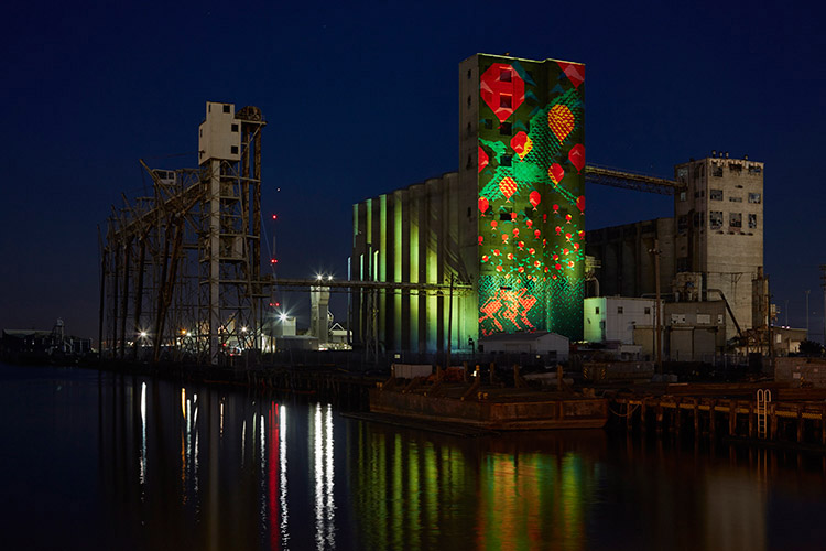 industrial building on the bay with green, red, orange projected onto the side of the building