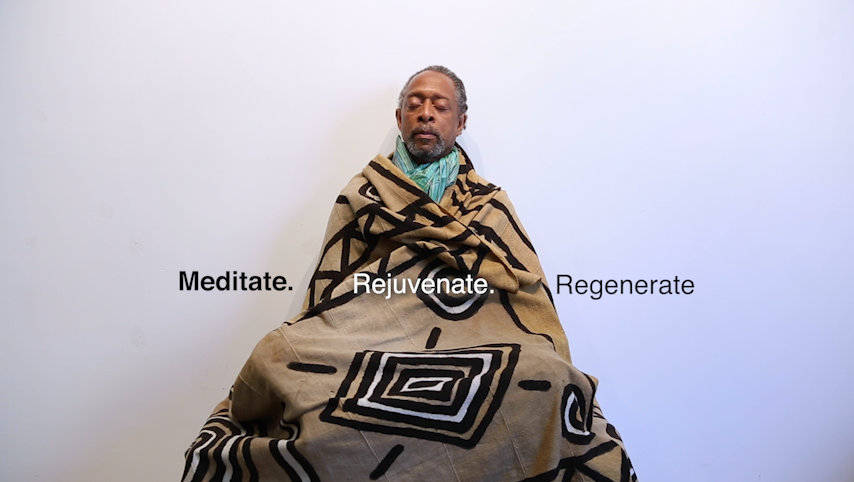A Black man sitting in the middle of the frame with his eyes closed. He is wrapped in a brown patterned blanket. Across the image are the words "Meditate. Rejuvenate. Regenerate."
