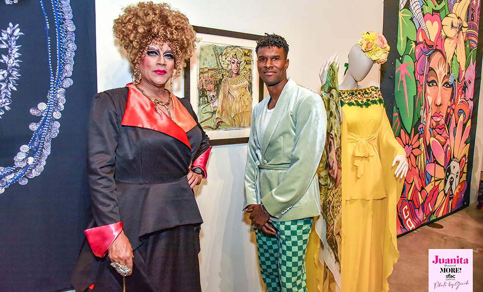 Image of drag queen Juanita MORE! and artist Serge Gay Jr. in front of a painting Serge made of Juanita.
