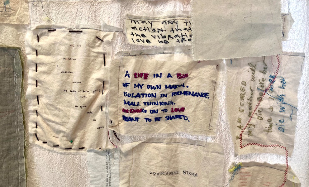 Image of textile with smaller pieces of fabric containing text in different languages sewn onto it. 