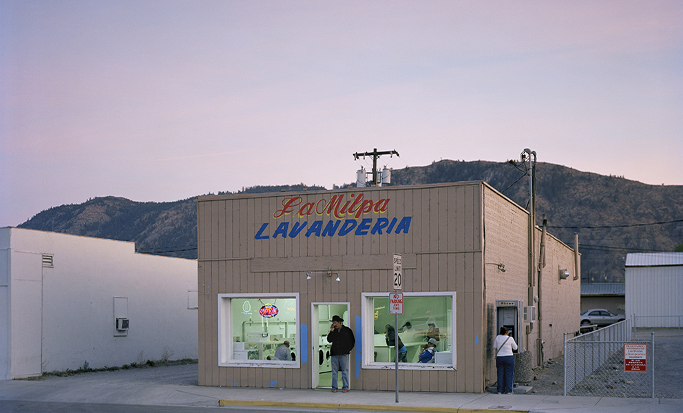 A man standing in front of a laundromat during the dusk. 