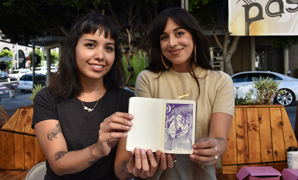 Two women hold up a passport with an artist-designed stamp