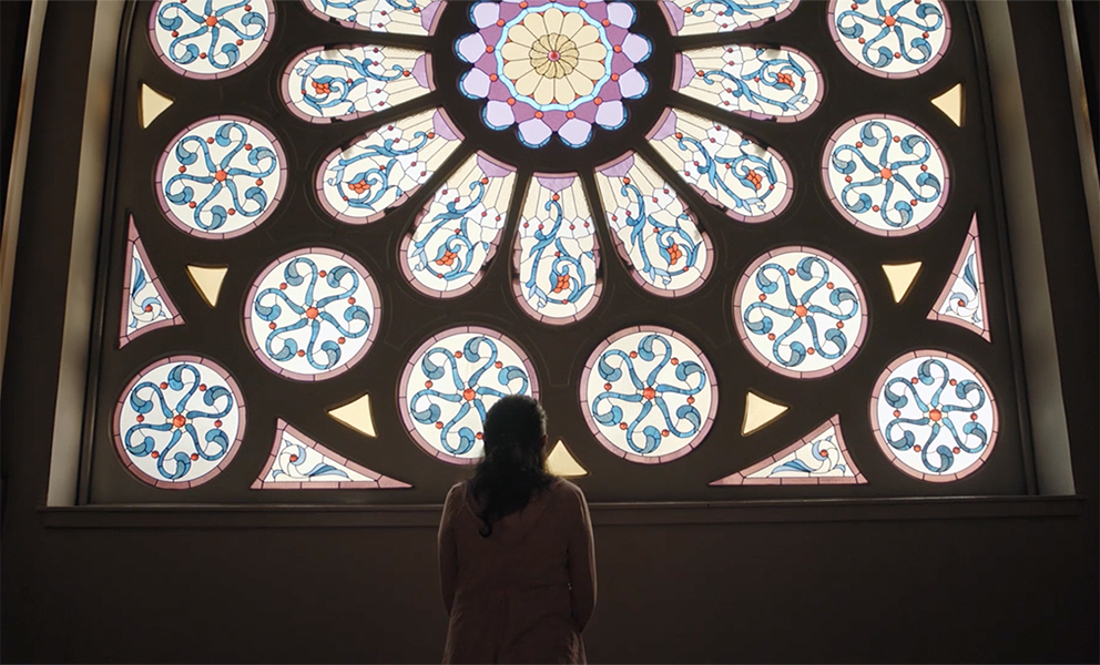 Image of woman standing facing a large stained glass window
