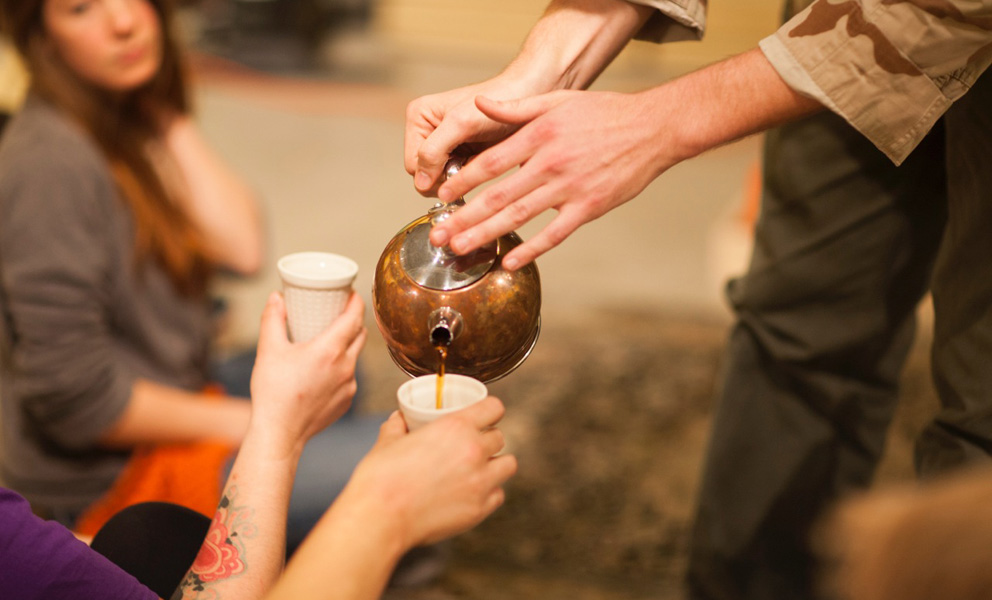 Hands pouring tea into a cup held by an outstretched hand