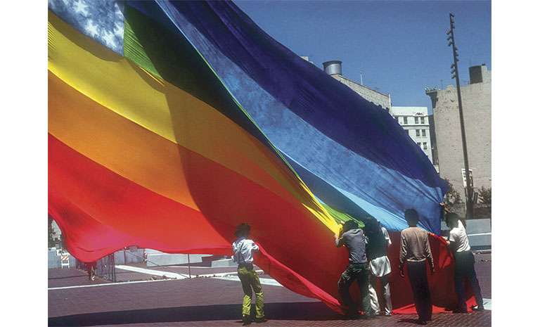 Five people raising a massive rainbow flag.