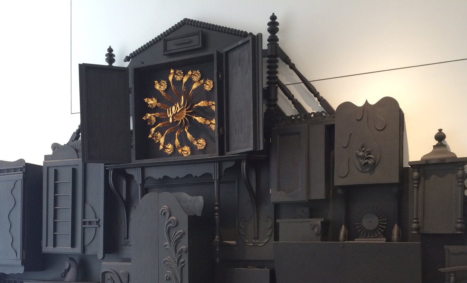 A collection of wood structures painted black. One is open to a collage of found objects. 