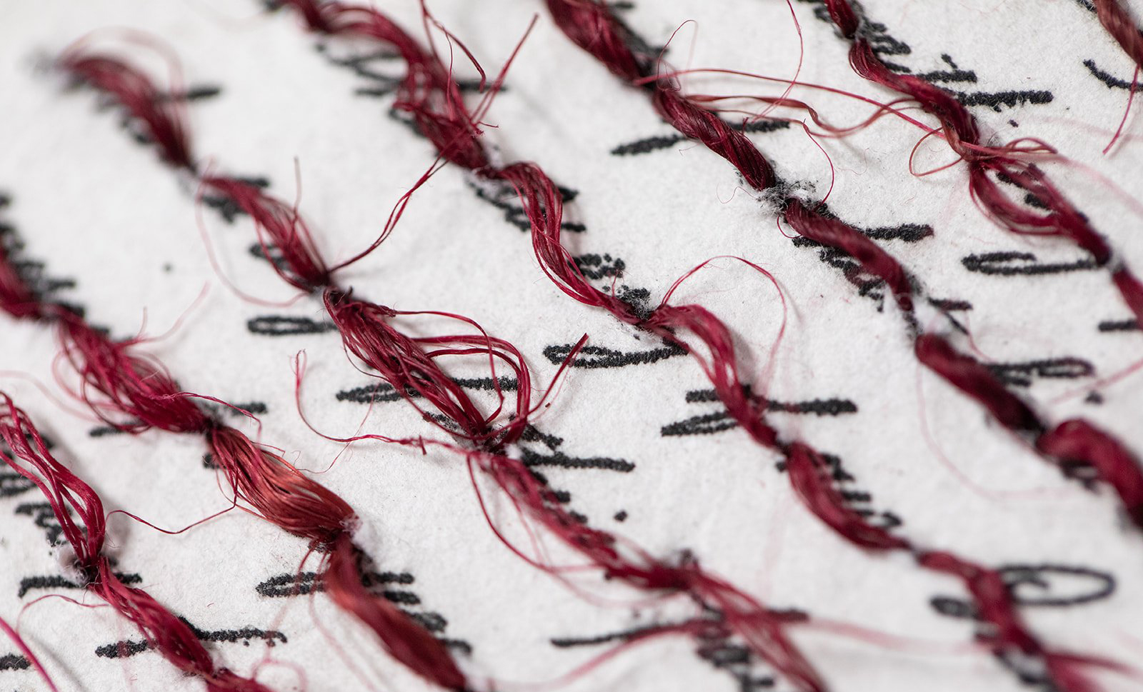A close up image of black script with red thread loosely stitched through them.