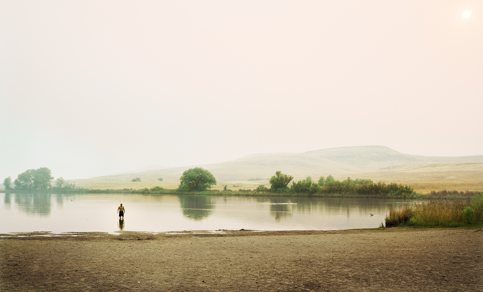 A wide shot of a lake with a man standing in the water