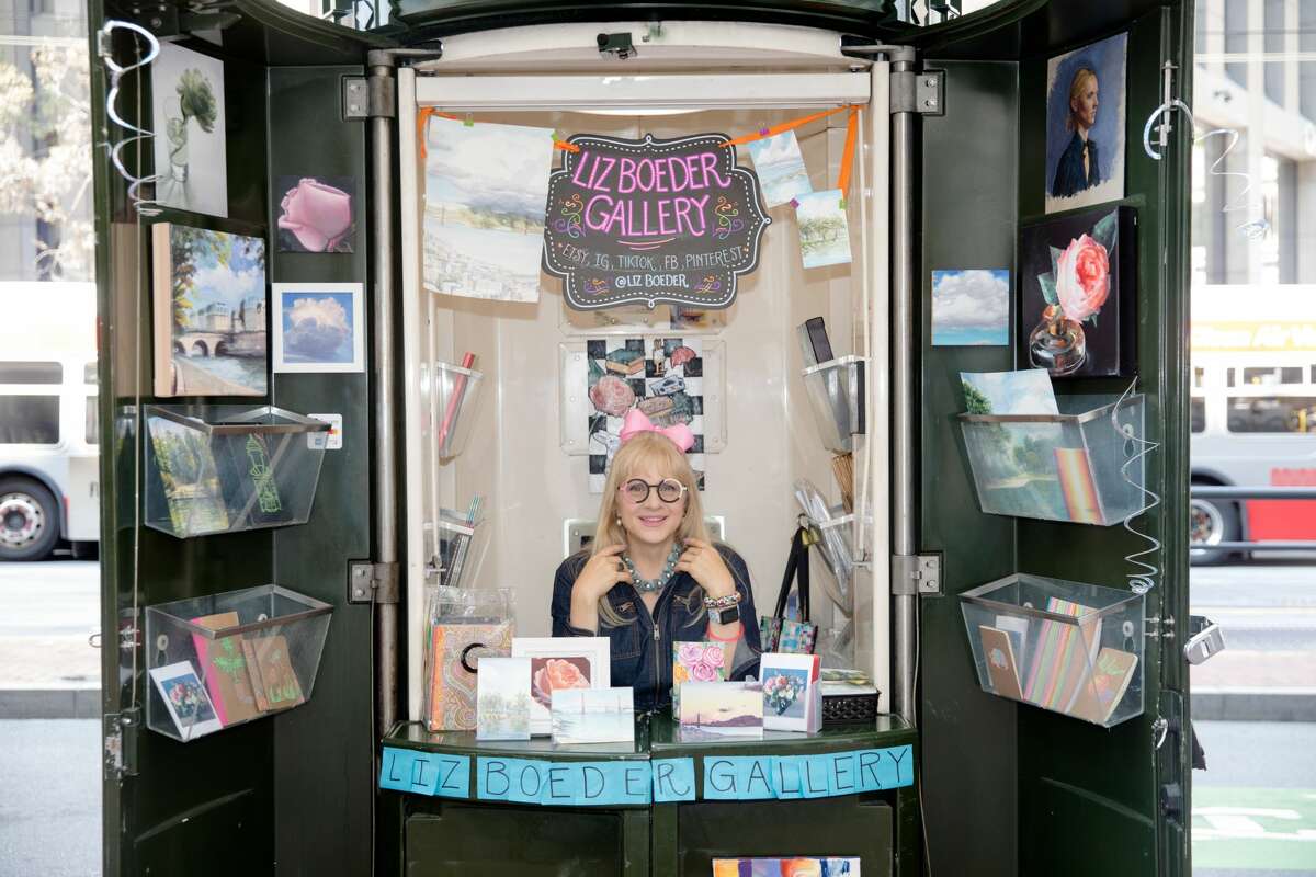 Image of an artist sitting inside a kiosk with their arts and crafts on display