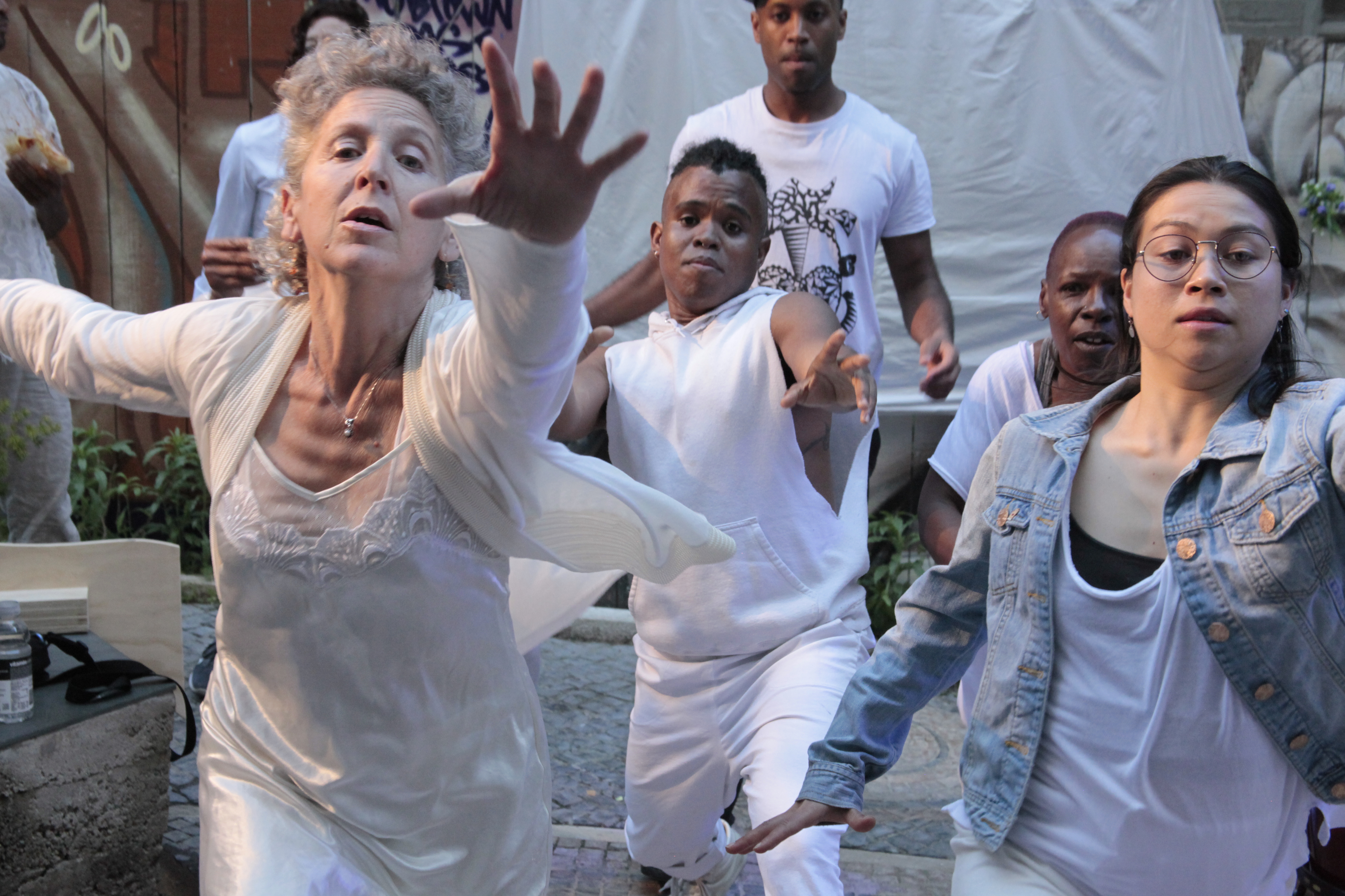 Dancers dressed in white performing in outdoor space reaching out towards the camera
