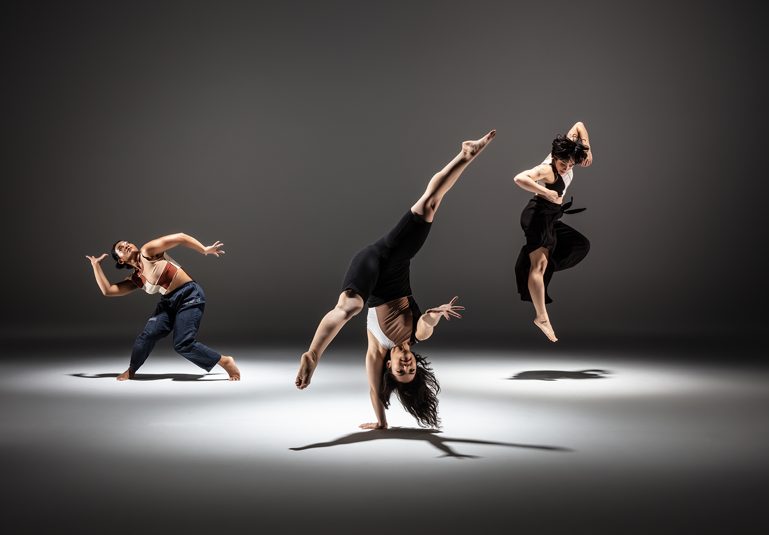 Three dancers in front of grey background in various poses.