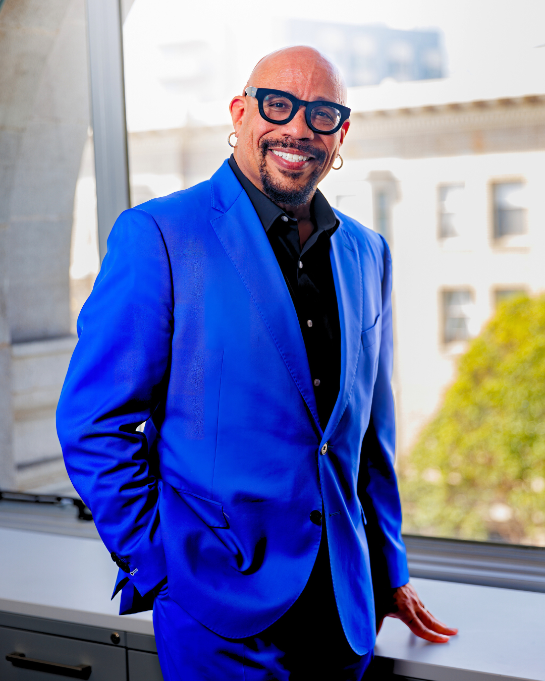 Image of Ralph Remington standing in front of a window wearing a blue suit. 
