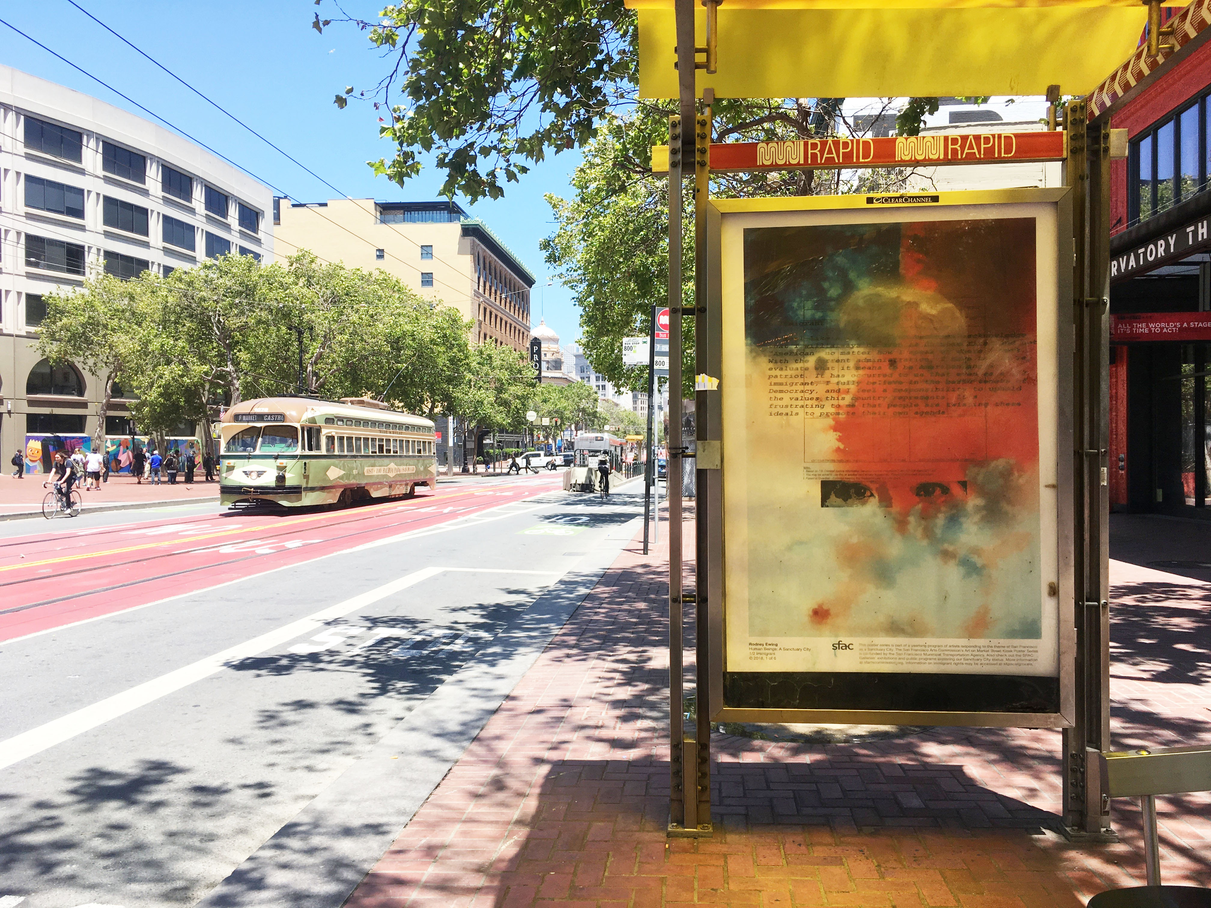 Poster on Market Street bus shelter, muni street car coming up the street