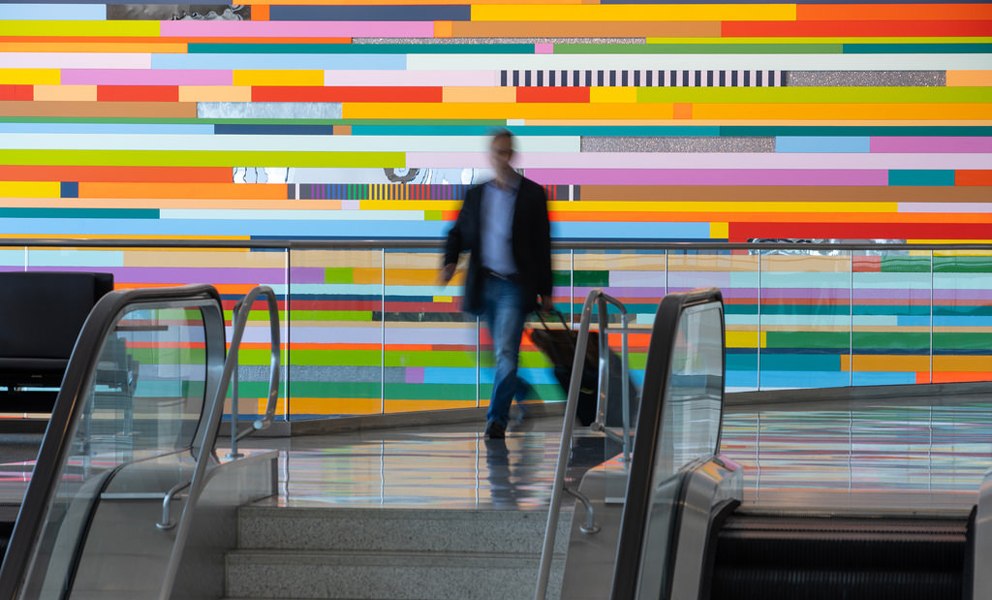 A man walking toward an escalator with a giant multi-colored mural behind him