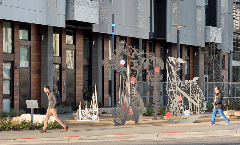 Stainless steel sculpture in the shape of a bear in front of an urban housing complex