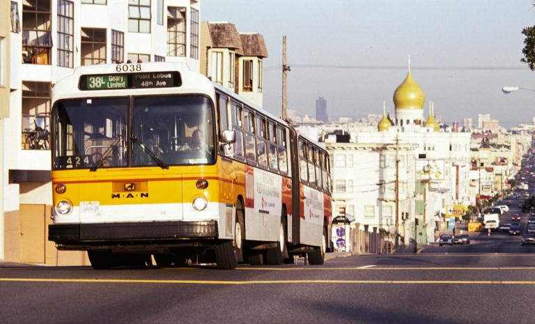 The 38-Geary bus driving down the street with a view of Geary street looking East. 